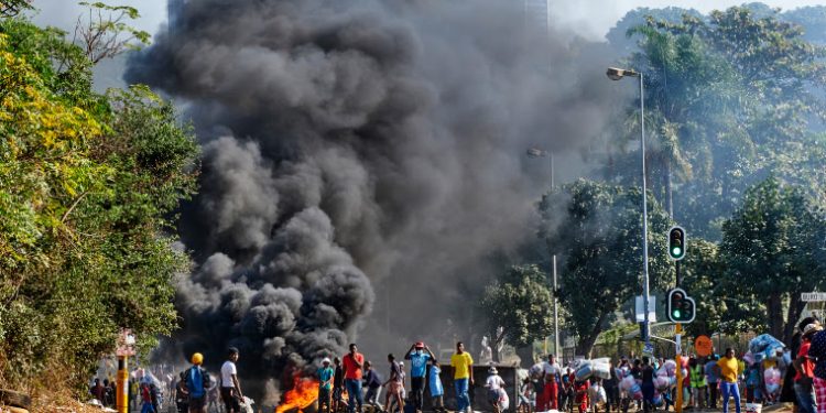Looters outside a shopping centre alongside a burning barricade in Durban, South Africa, Monday July 12, 2021. Police say six people are dead and more than 200 have been arrested amid escalating violence during rioting that broke out following the imprisonment of South Africa's former President Jacob Zuma. (AP Photo/Andre Swart)